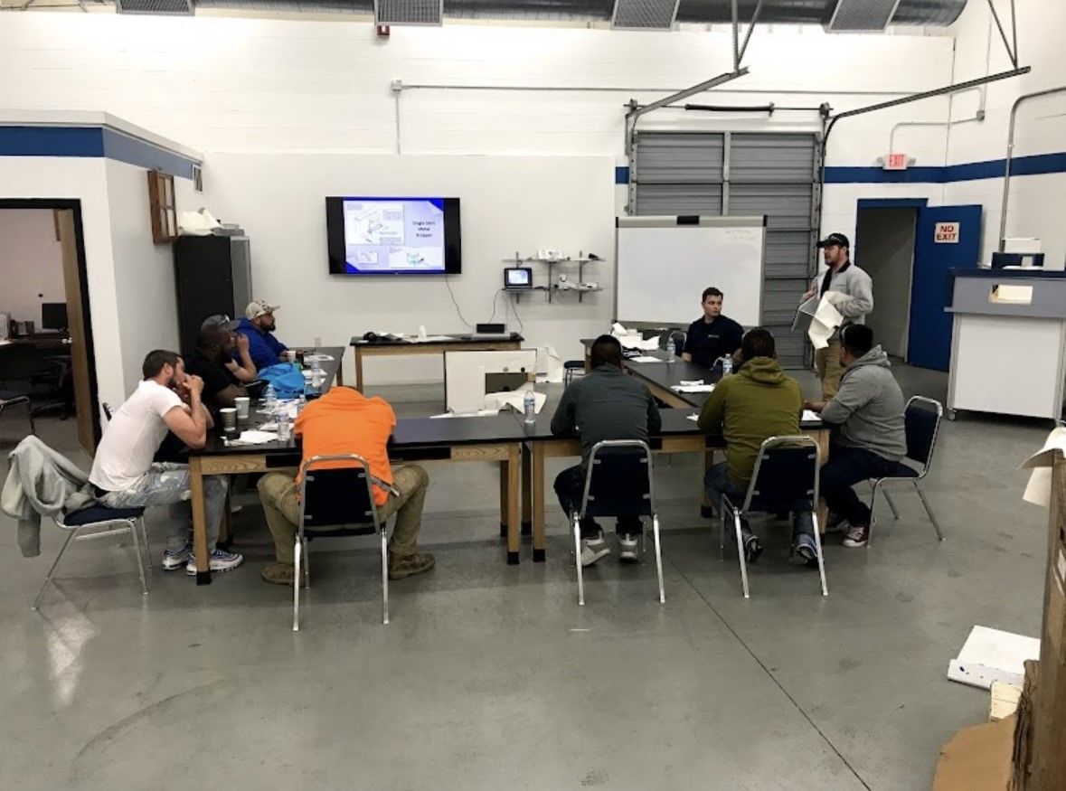 People seated around tables in a workshop room, watching a presentation on a wall-mounted screen.