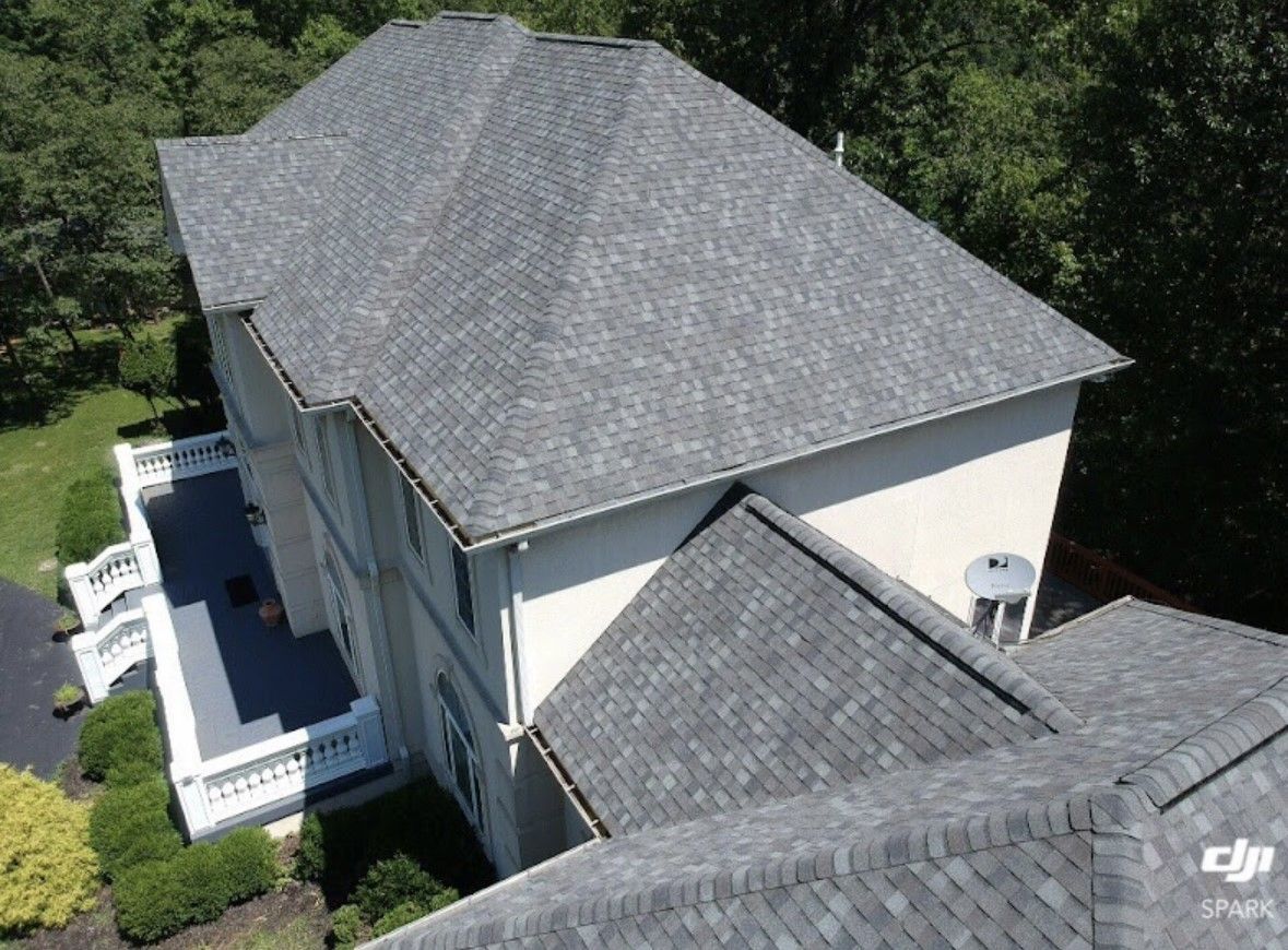 Aerial view of a house with gray shingle roofs surrounded by trees and a driveway