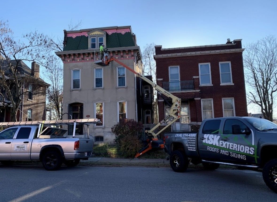 Workers repairing roof on a beige townhouse with two trucks parked outside.