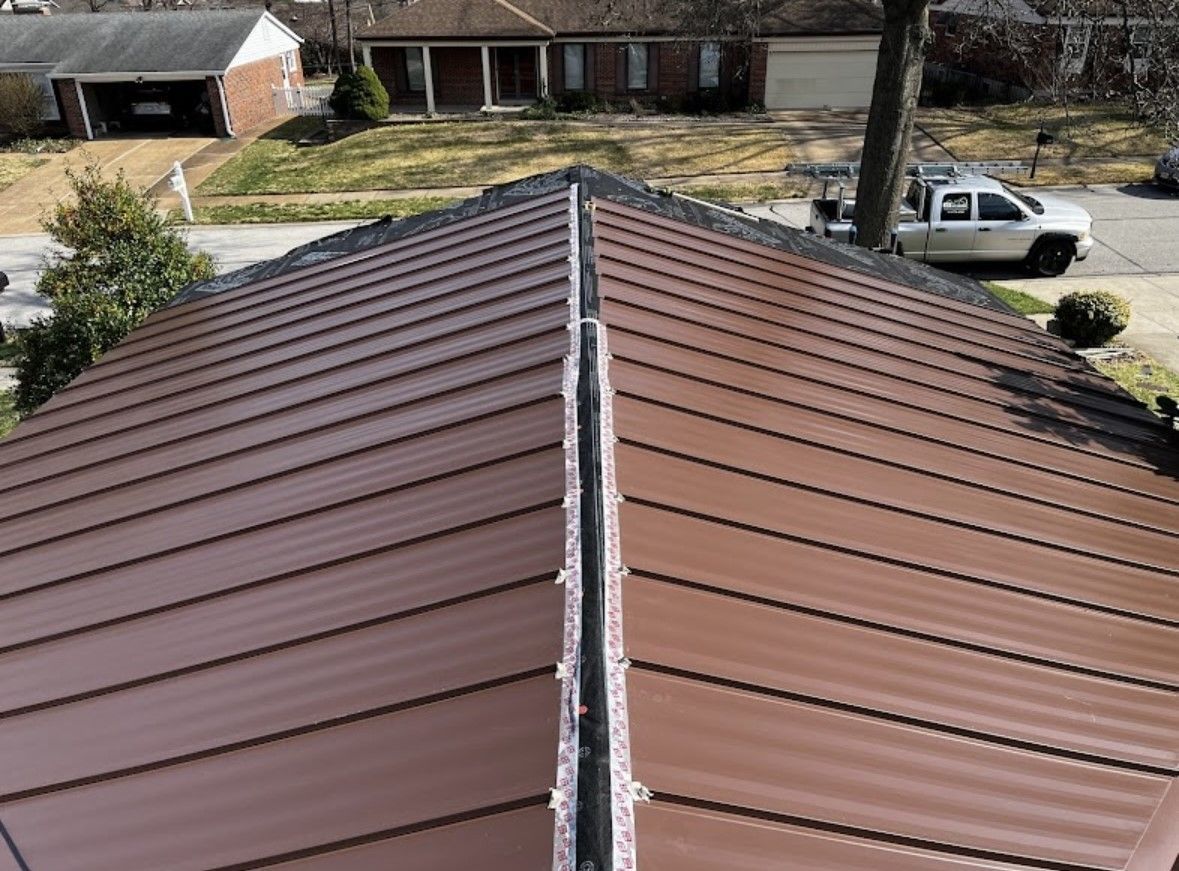 Brown metal roof viewed from above with a central ridge and houses in the background