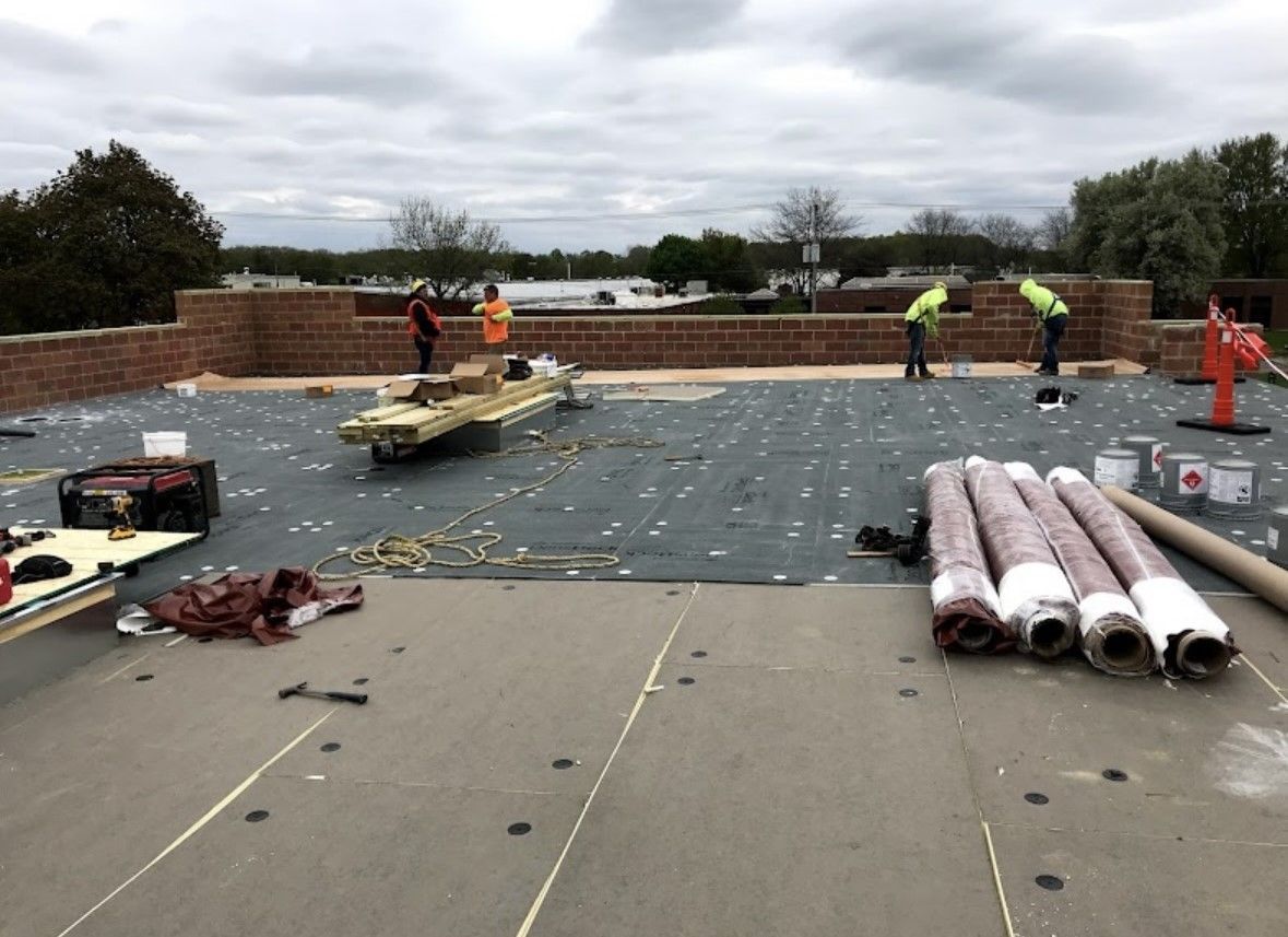 Roof workers installing materials on a flat roof under cloudy skies