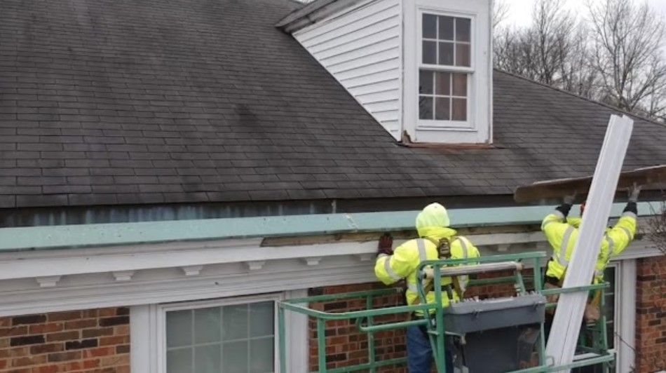 Workers in neon jackets on a roof repairing gutters beside a brick building