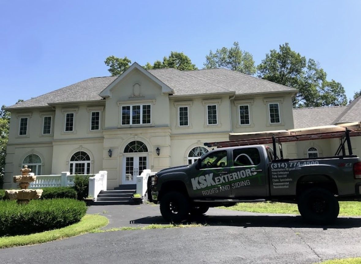 Large two-story white house with a black pickup truck parked in the driveway under a clear blue sky