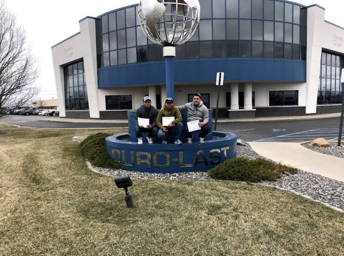 Three people stand by a EuroLast sign outside a modern office building with a globe sculpture.