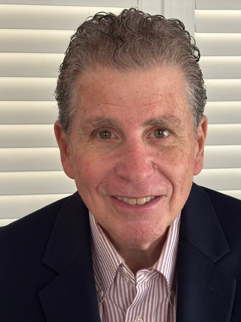 A man in a suit and striped shirt is smiling in front of a window.