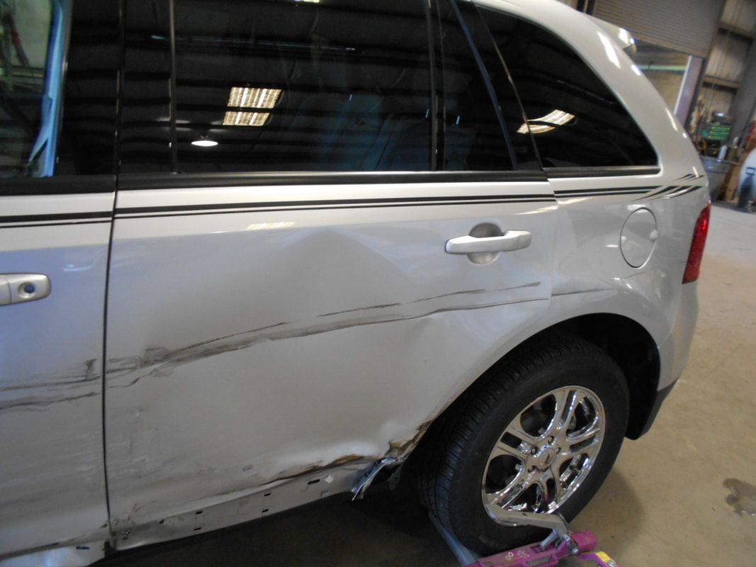 A silver car with a damaged fender is parked in a garage