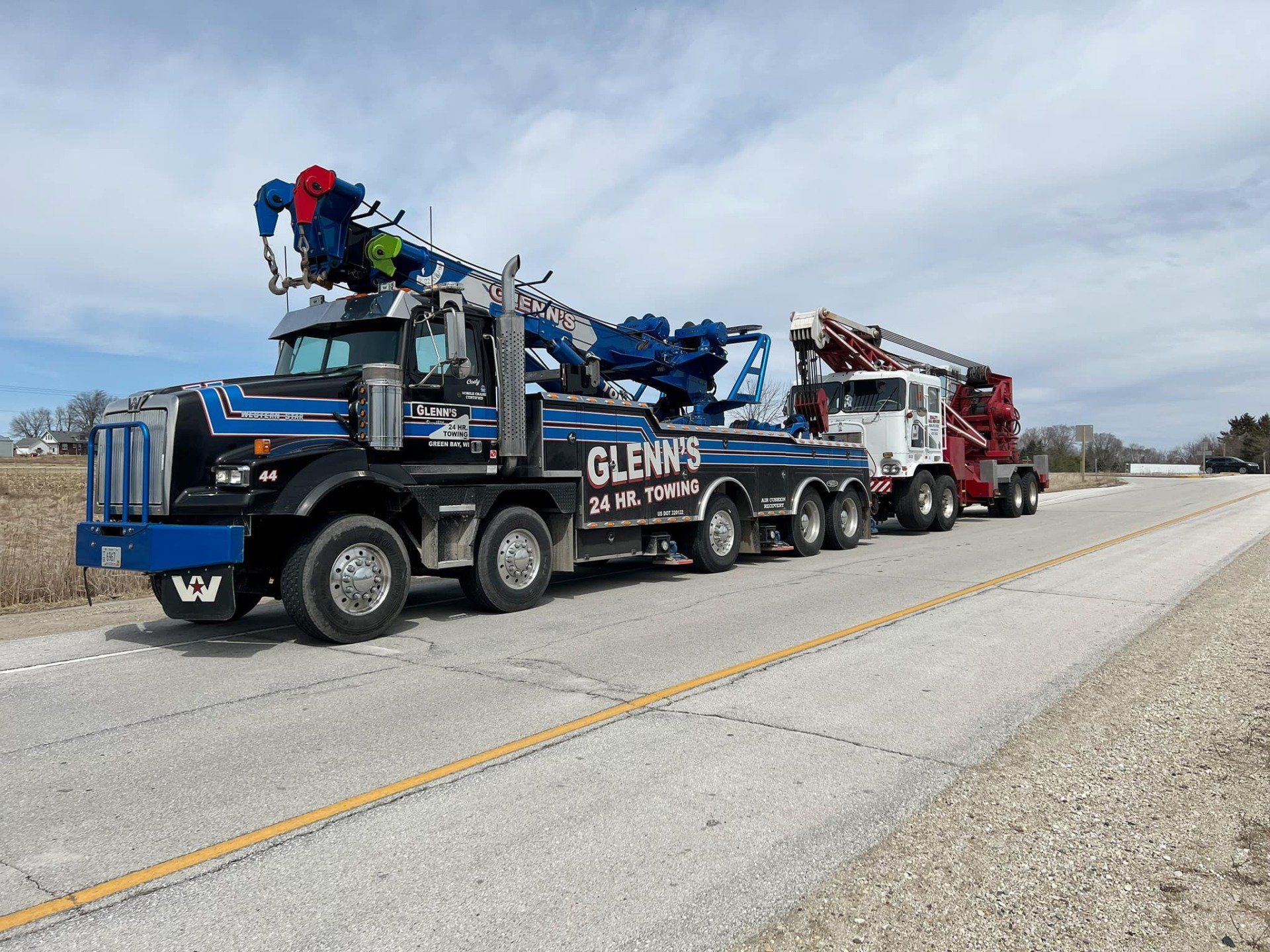 A large black and blue tow truck towing a red tow truck on a highway under a blue sky.