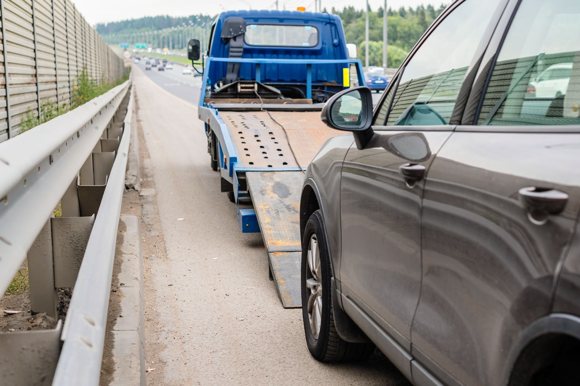 Blue flatbed tow truck loading a gray SUV on a highway shoulder
