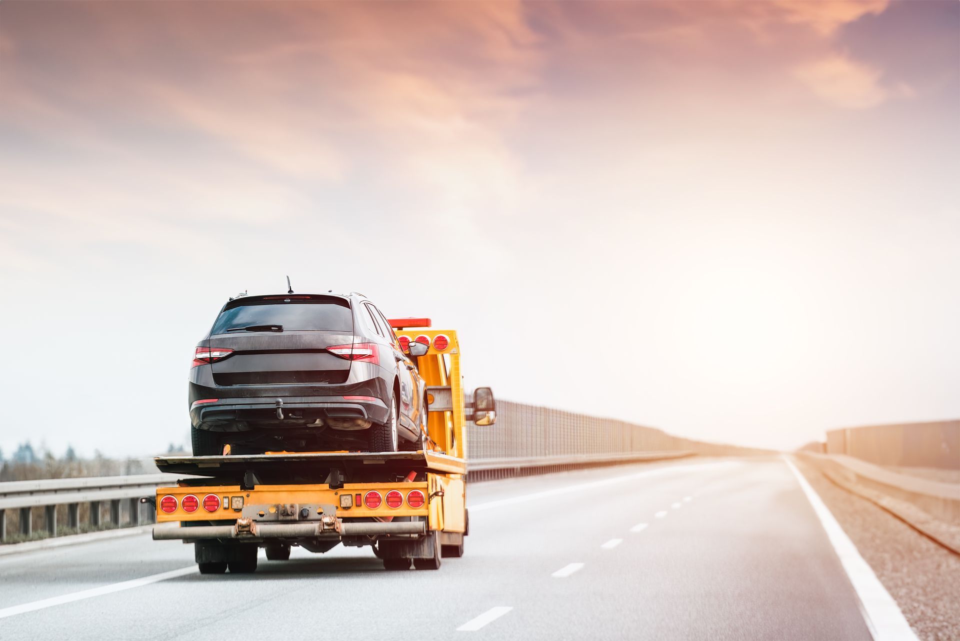 A car is being towed on a flatbed truck on a highway.