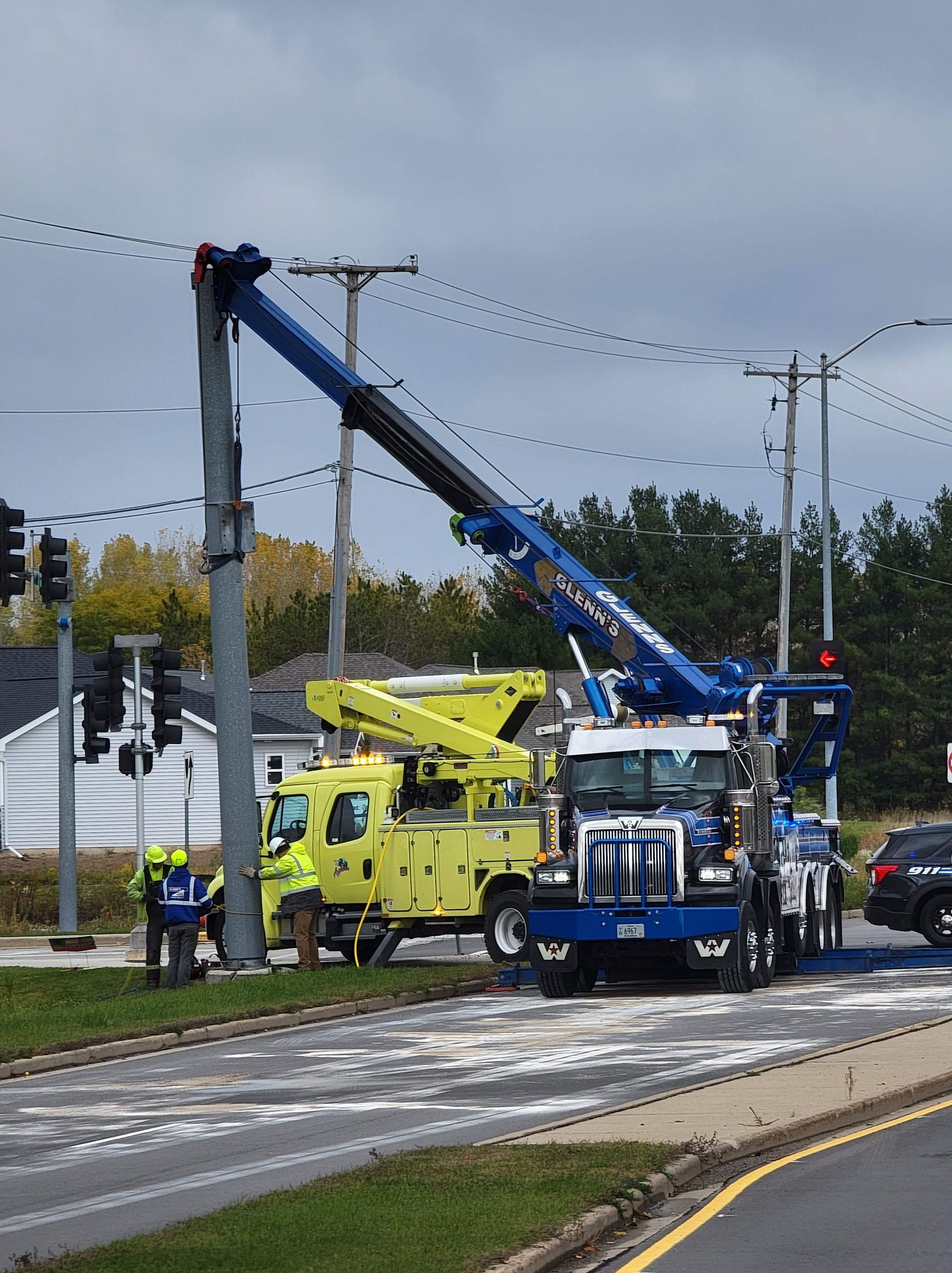 Two utility trucks working on a pole next to a road, one with a raised boom.