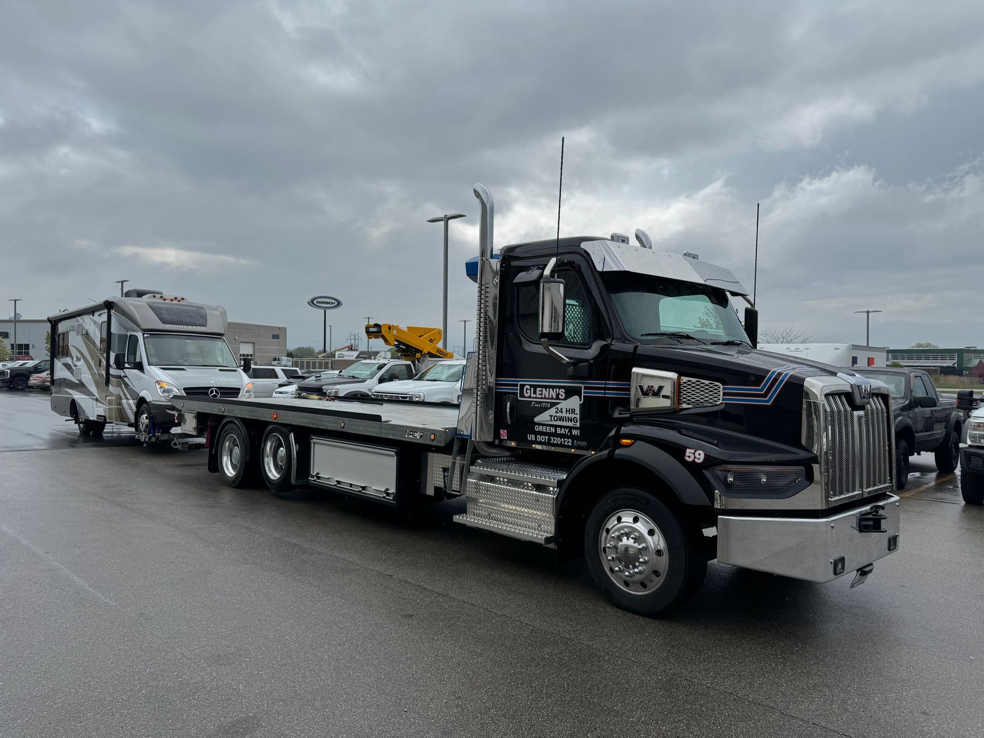 Black tow truck towing a white RV on a wet, gray day.