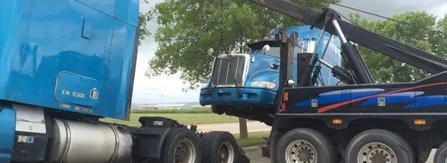 Blue semi truck being towed by a tow truck on a sunny day.