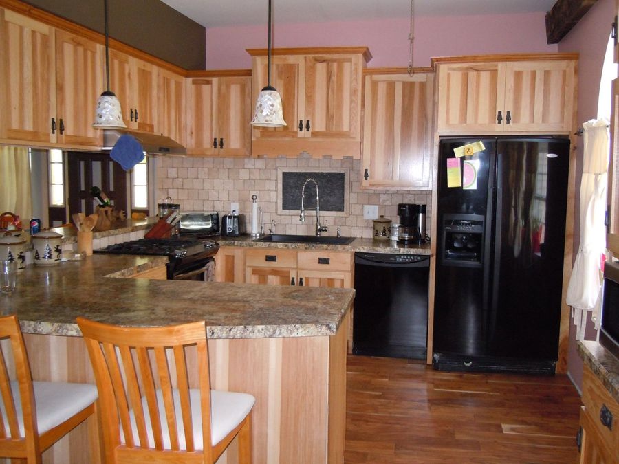 Kitchen with light wood cabinets, granite counters, black appliances, and bar seating.