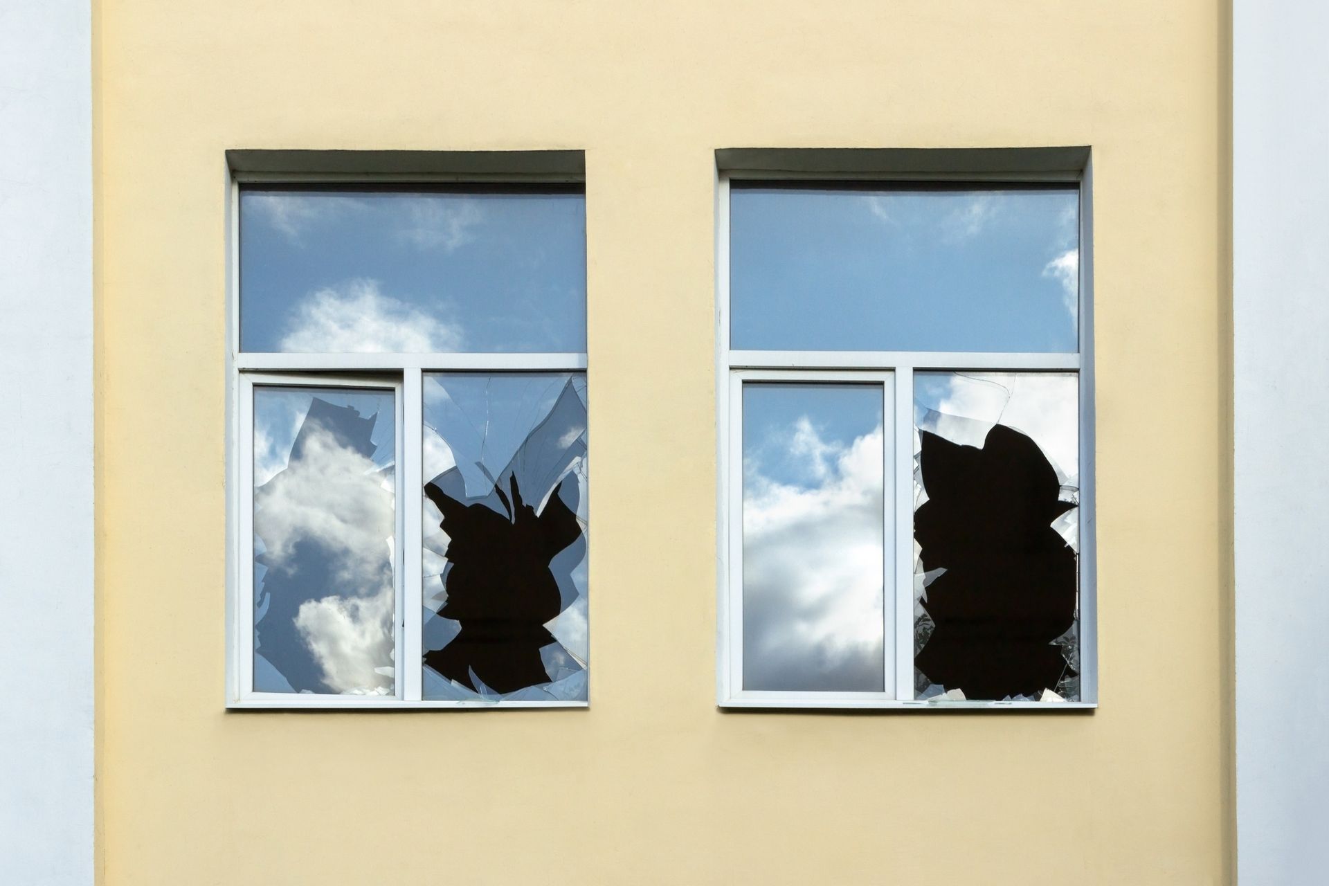 Two broken windowpanes reflect a moody, overcast sky.