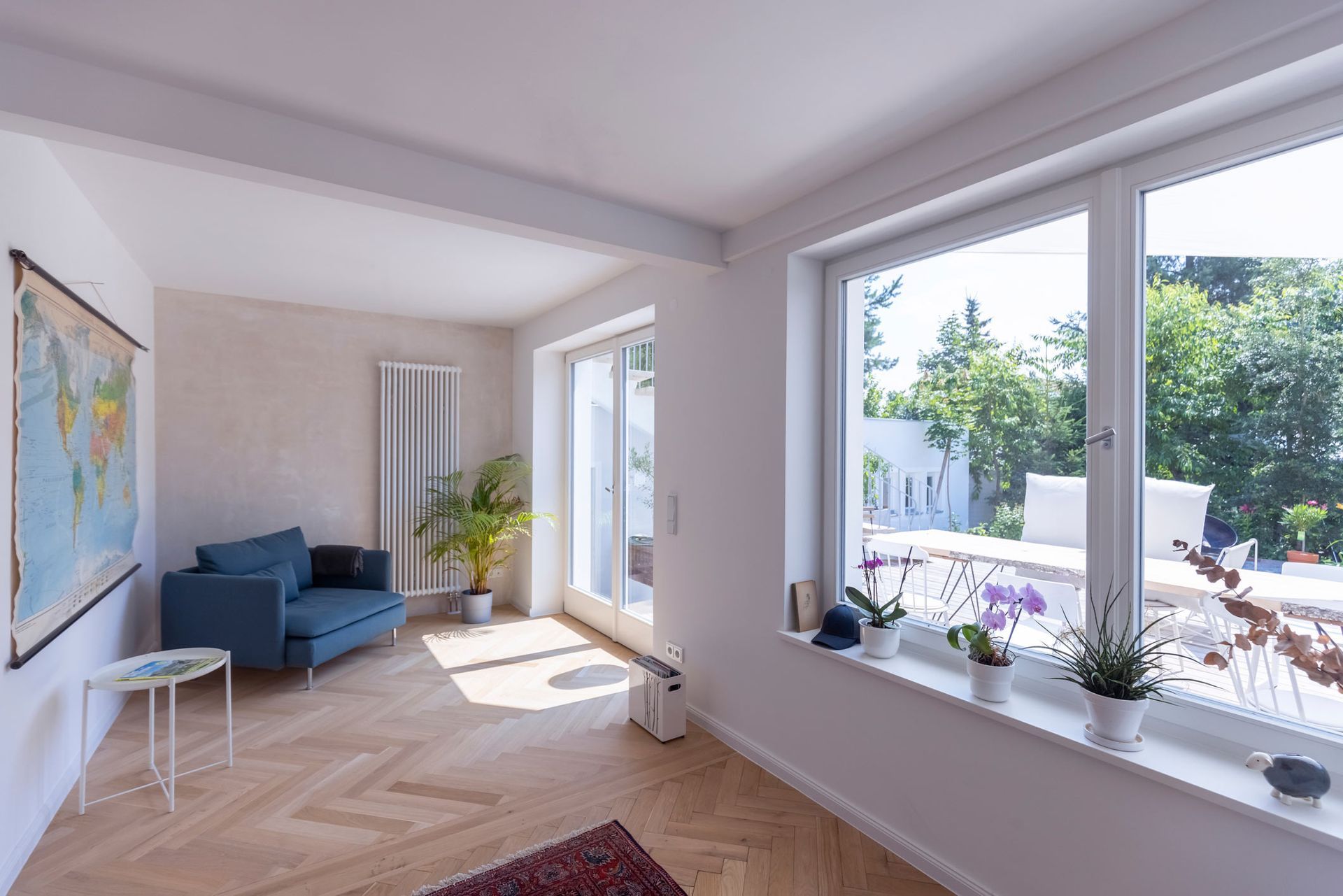 Bright, light-filled room with large windows, blue sofa, wooden floor, and a world map on the wall.