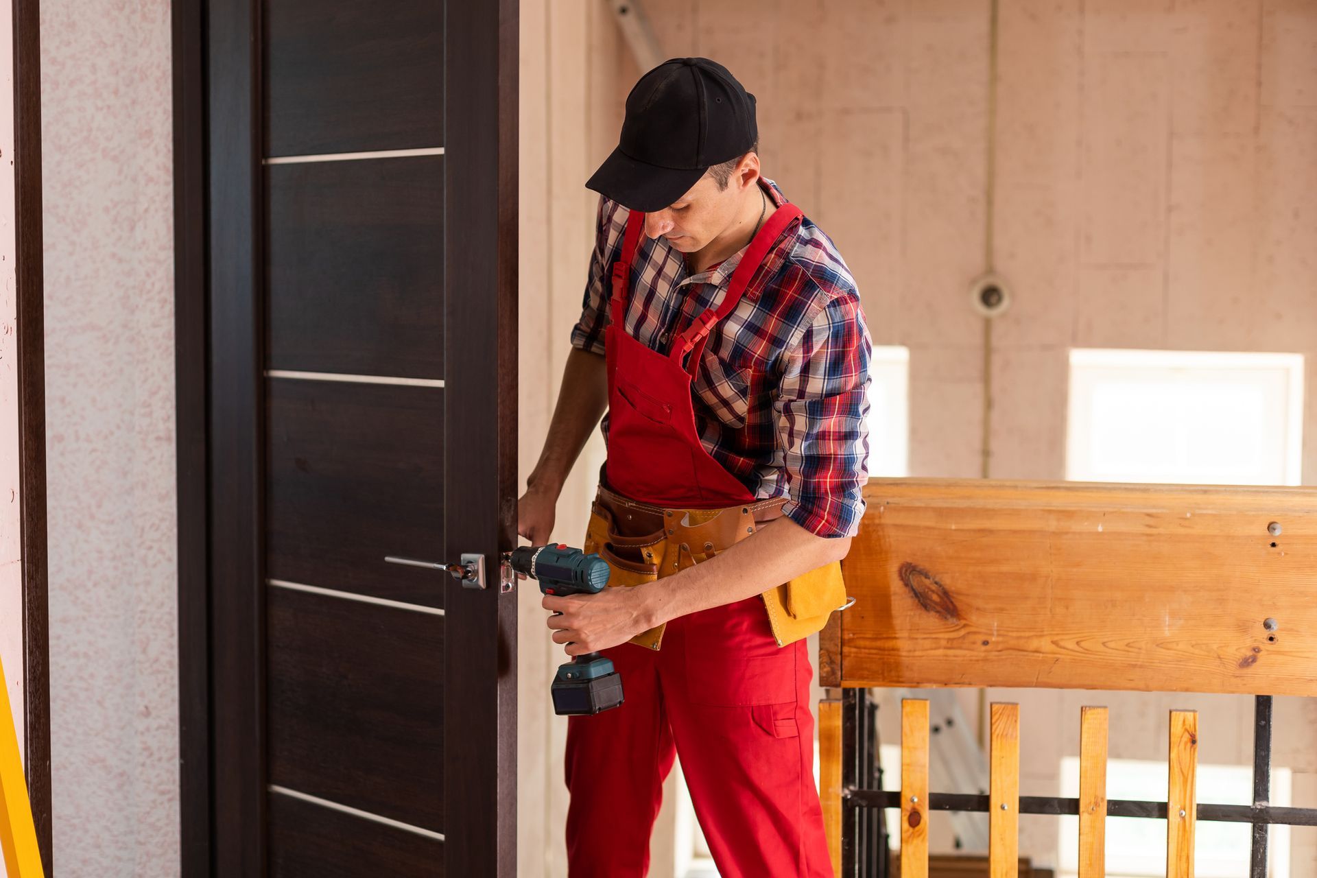 Handyman in red overalls using a drill to install a door lock.