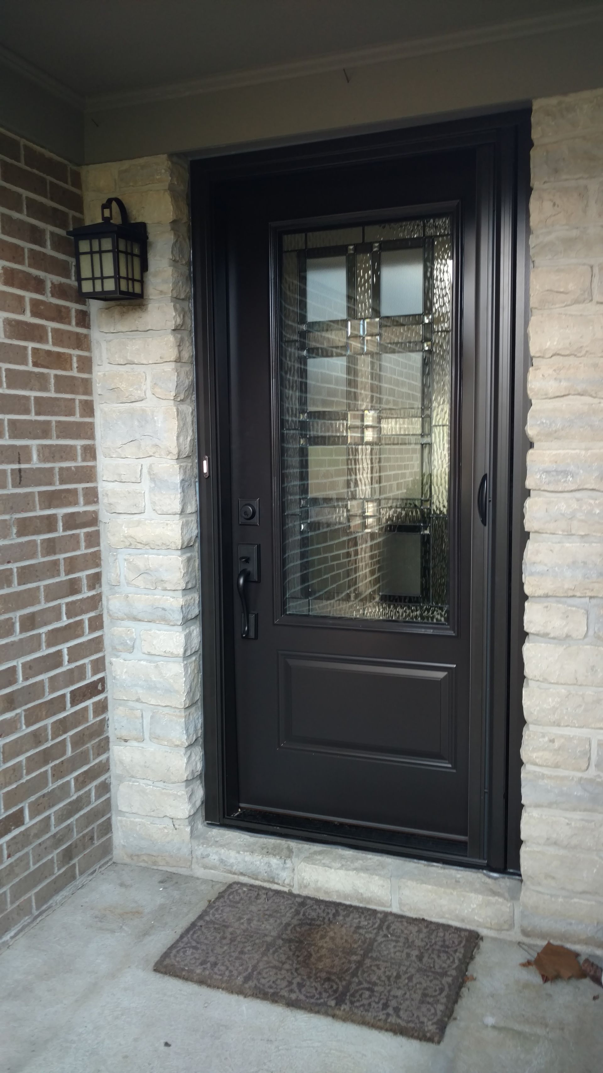 Dark brown door with glass panel and decorative trim, set in brick and stone wall.