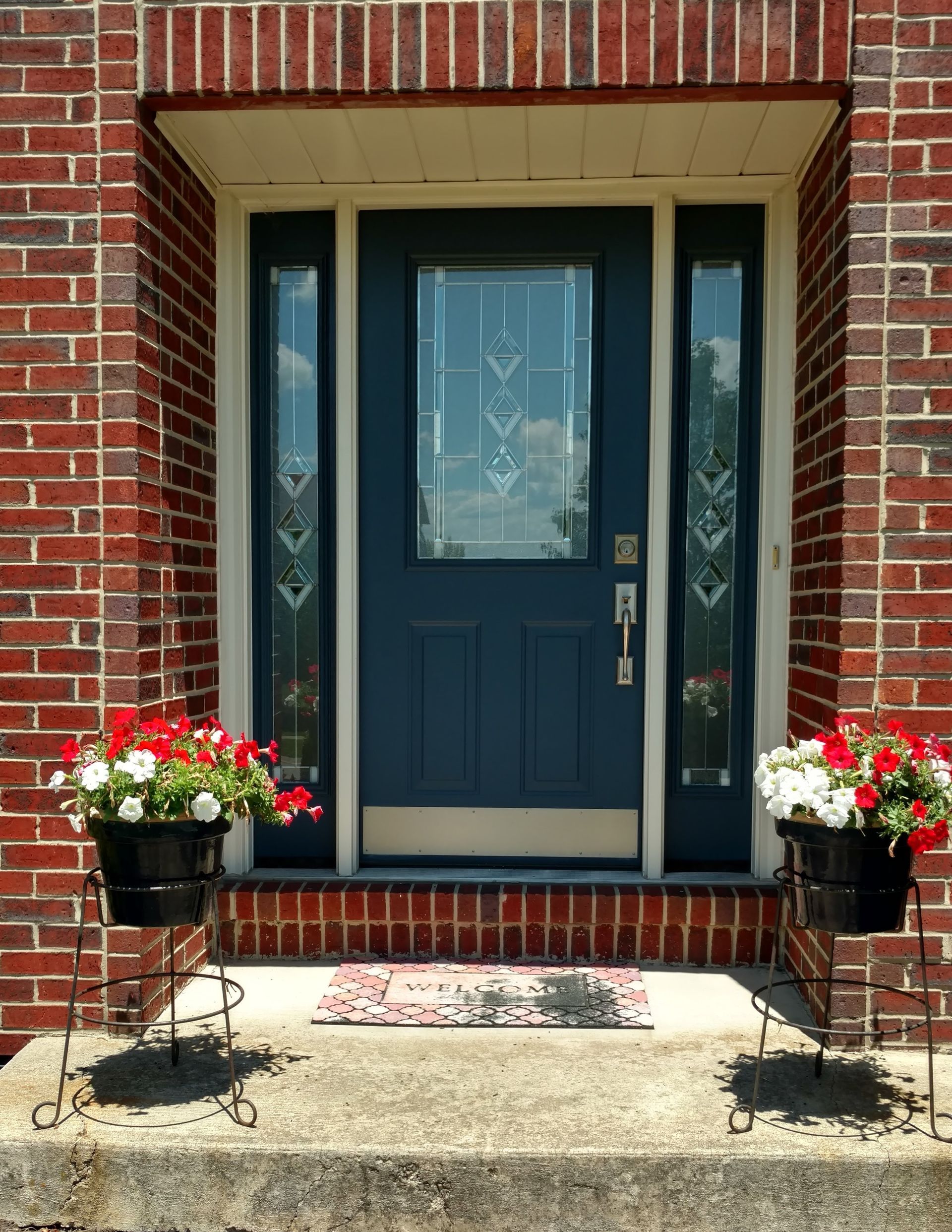 Beautiful patio door installed in a residential property. Blue front door with glass panels framed by red brick, flower baskets on either side.