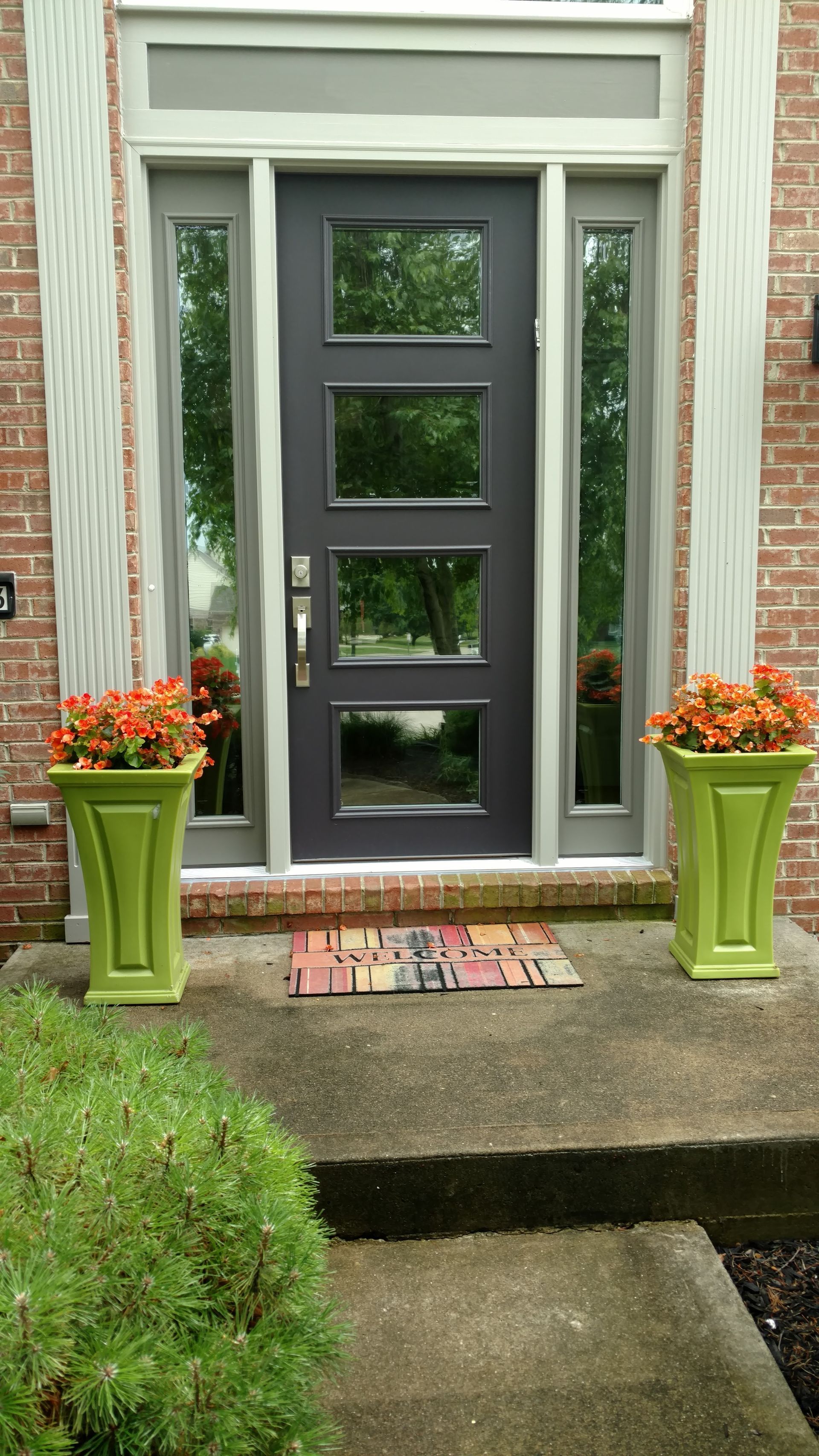 Gray front door with glass panels, green planters with orange flowers, brick exterior.