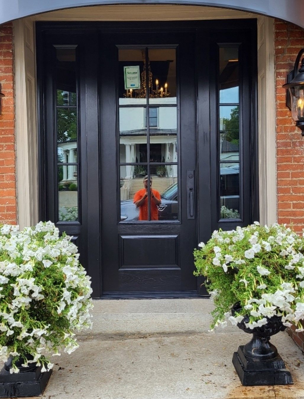 Black front door with sidelights, flanked by white petunia-filled planters.