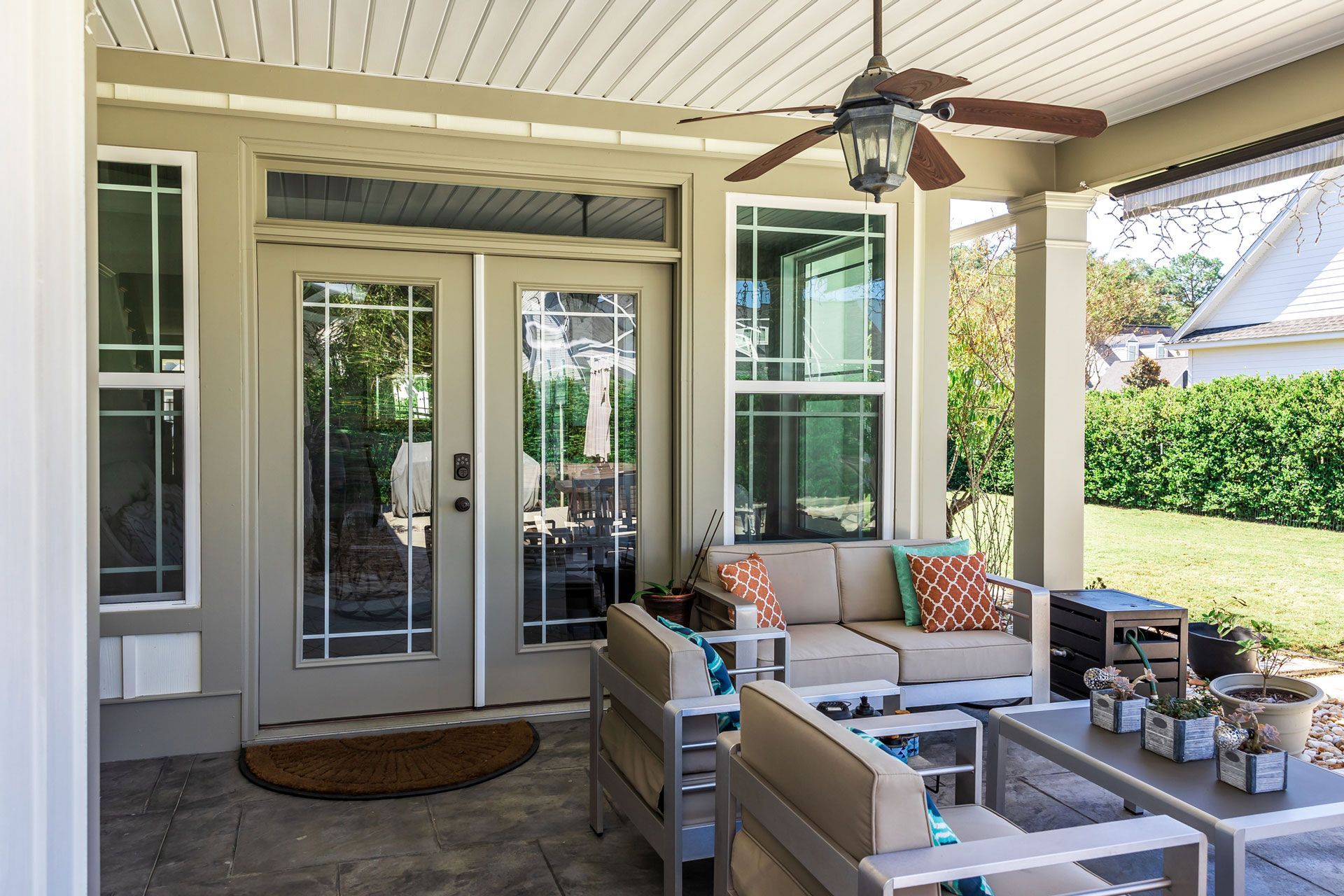 Covered patio with seating, French doors, and ceiling fan; overlooking a green yard.