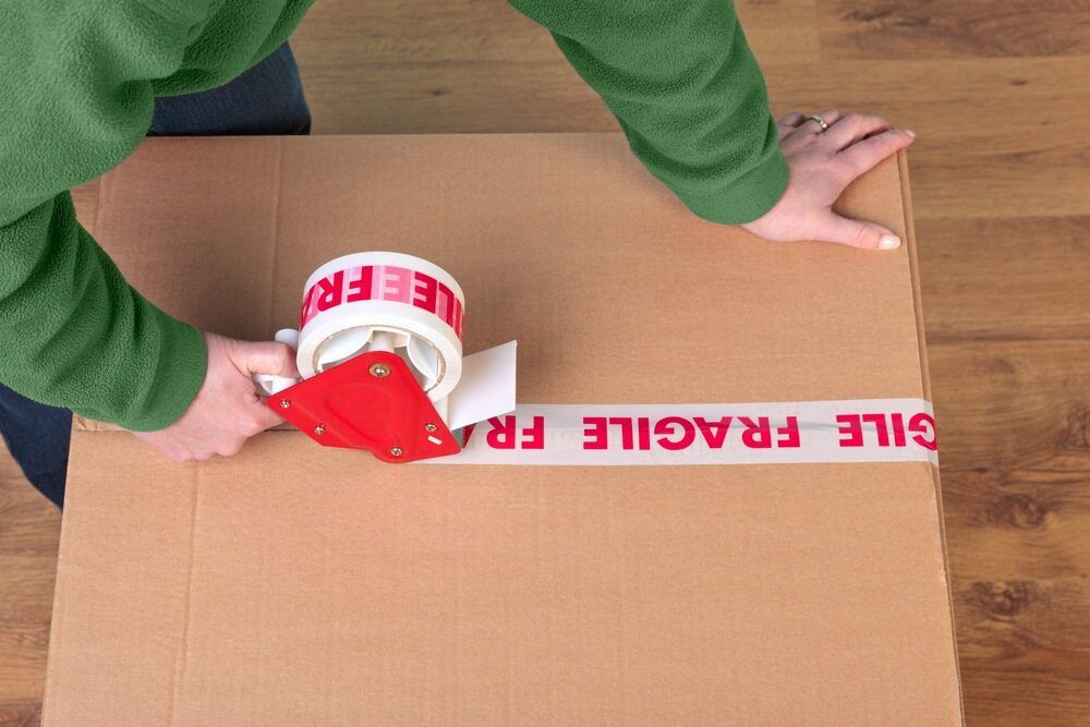 A Person is Wrapping a Cardboard Box With Fragile Tape — Wide Bay Removals In Dundowran, QLD