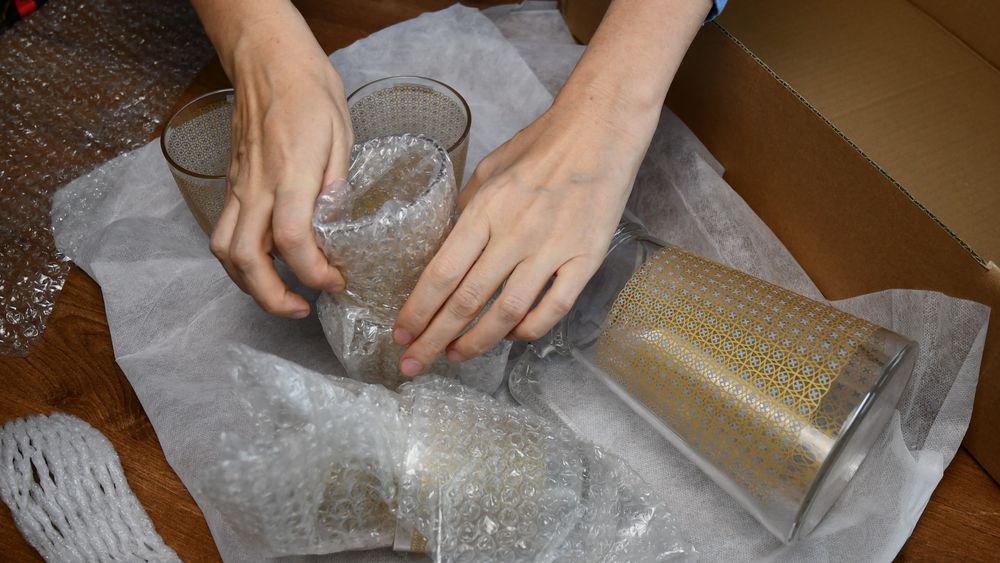 A Person is Wrapping Wine Glasses in Plastic Bubble Wrap — Wide Bay Removals In Dundowran, QLD