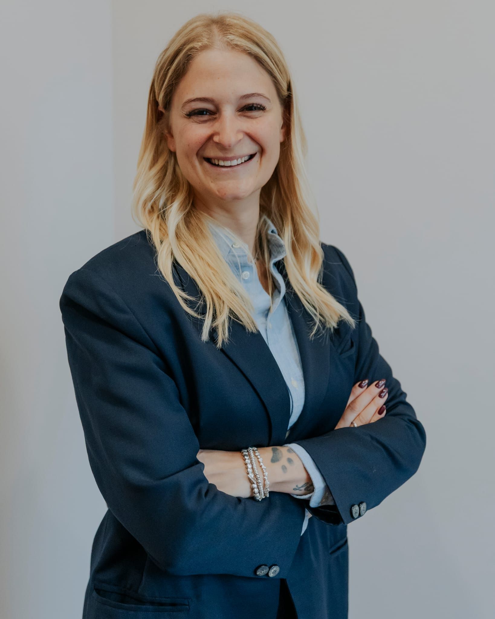 Donna sorridente con blazer blu scuro e braccia incrociate su sfondo grigio