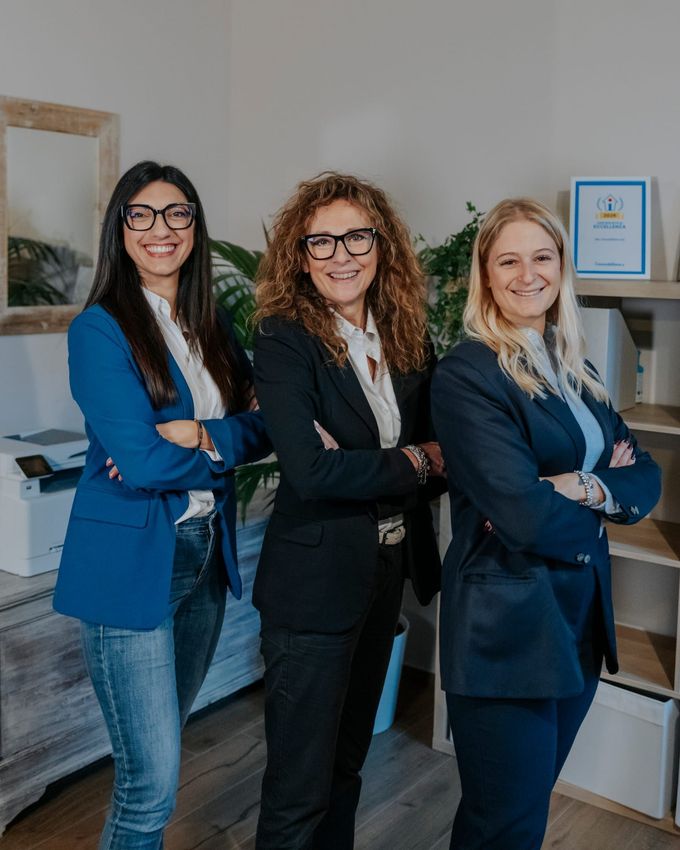 Tre professionisti in abiti da lavoro, in piedi insieme in un ufficio, con le braccia incrociate e un sorriso stampato in faccia.
