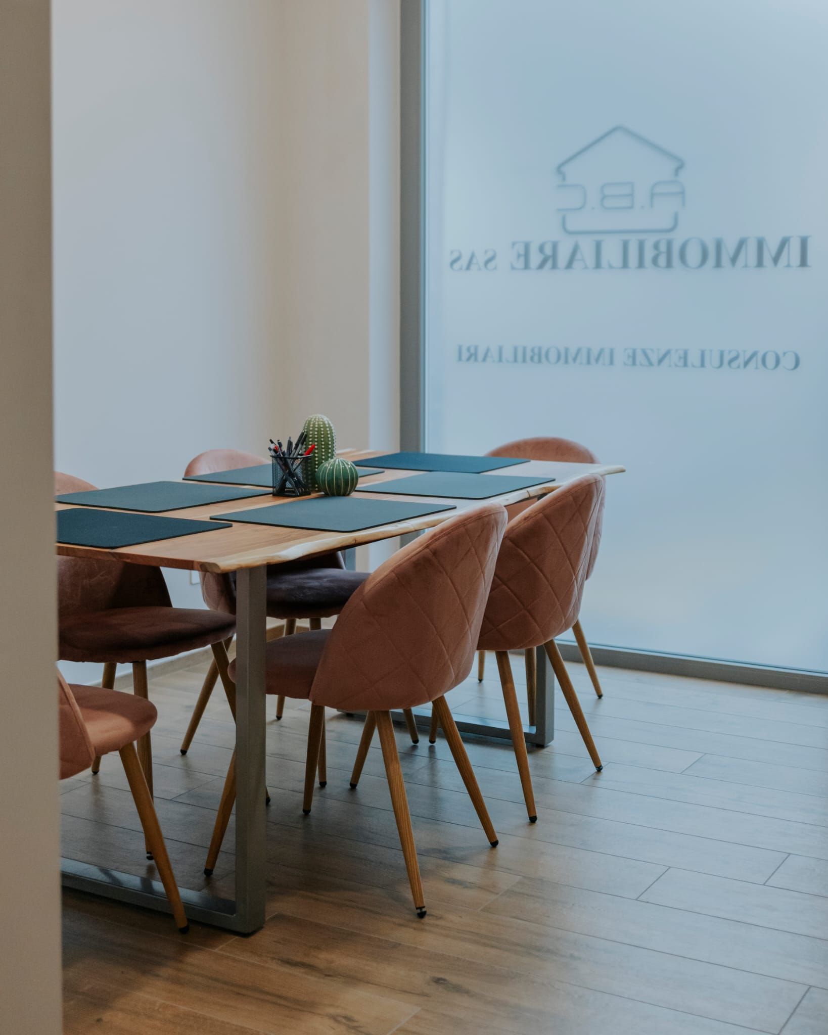 Sala riunioni moderna con tavolo in legno, sedie color cuoio e parete in vetro satinato con logo aziendale.