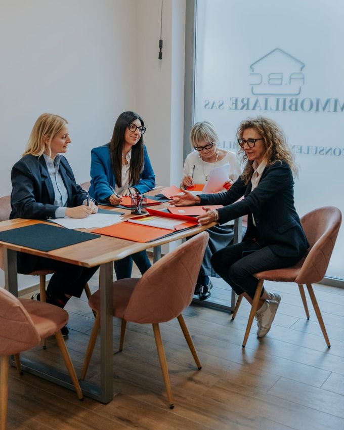 Quattro colleghi siedono attorno a un tavolo in una sala riunioni con pareti di vetro, esaminando documenti e discutendo di lavoro.