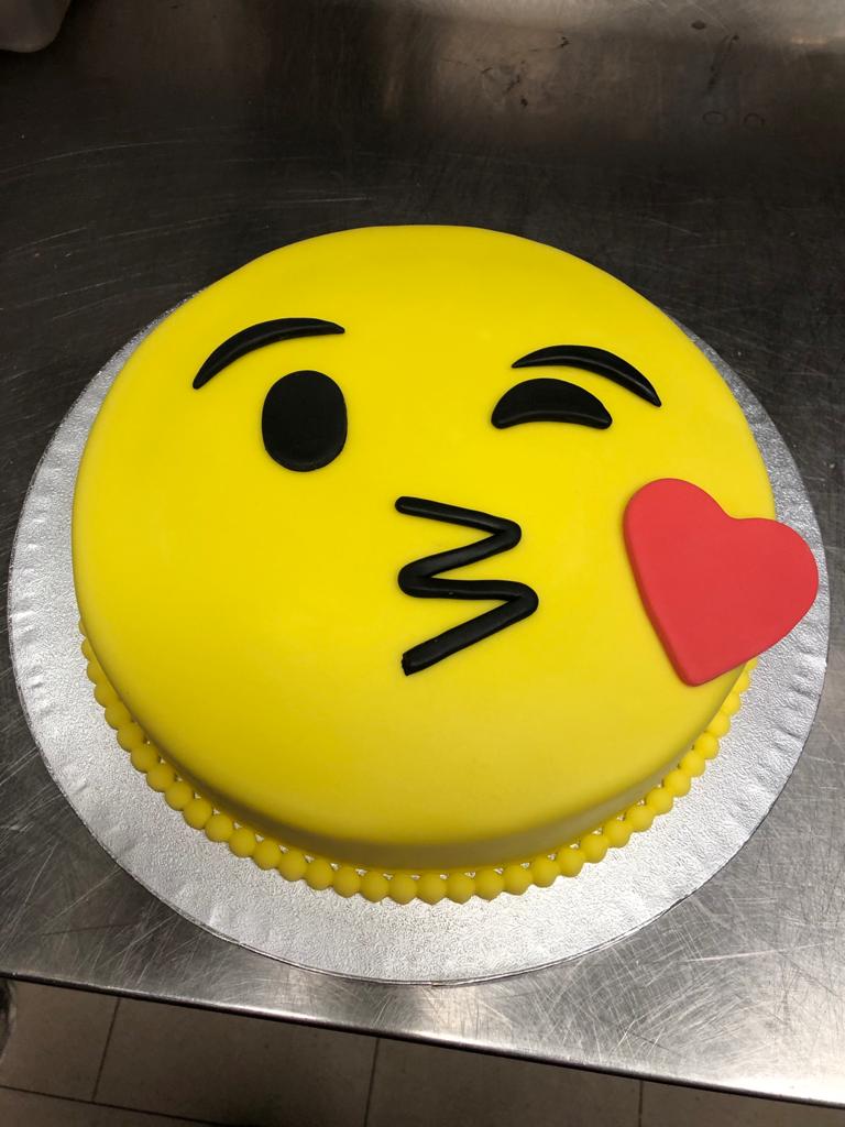Una torta gialla con una faccina sorridente e un cuore rosso sopra