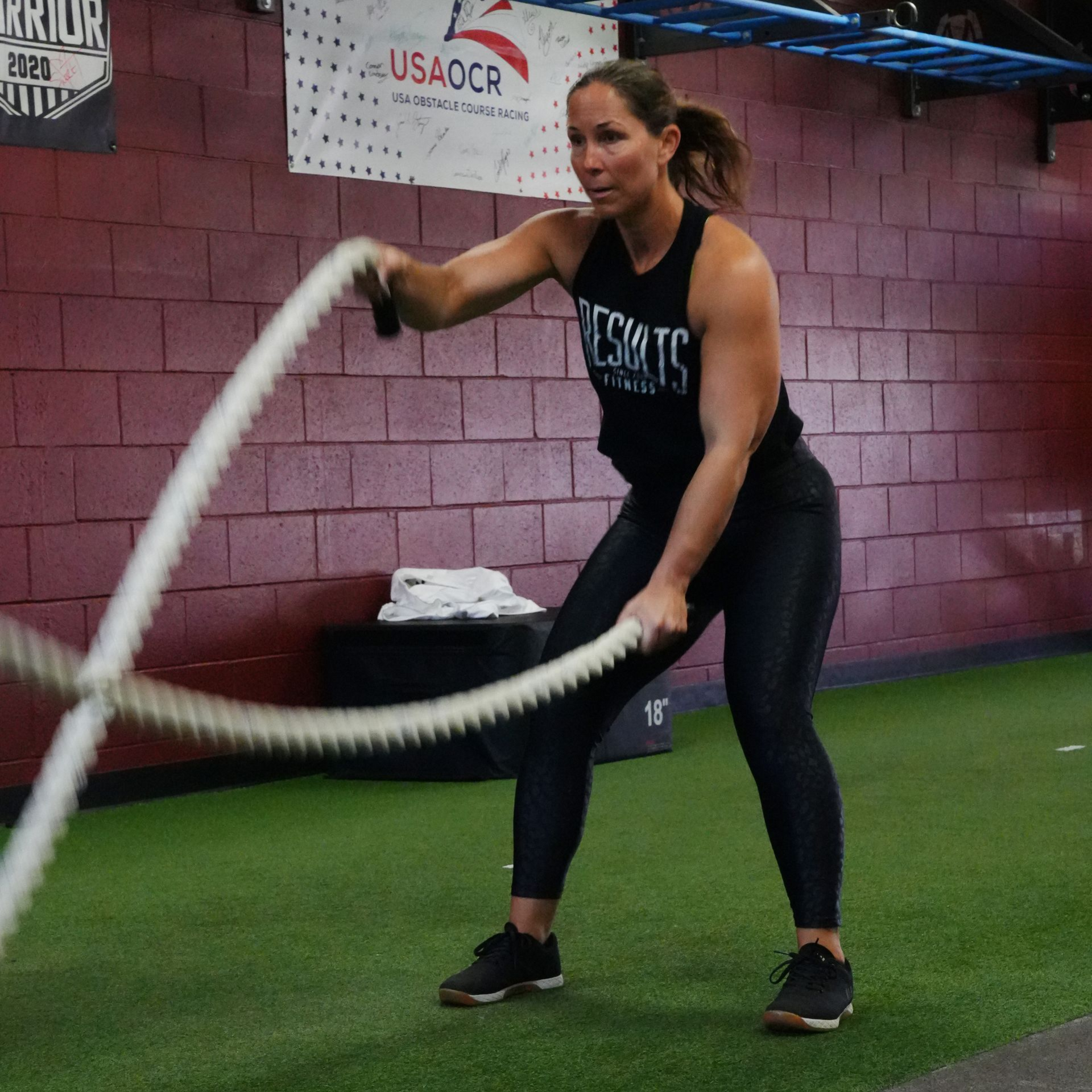 Woman working out with battle ropes in a gym; swinging ropes with energy.