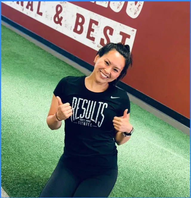 Woman in black shirt giving thumbs up in a gym with the word