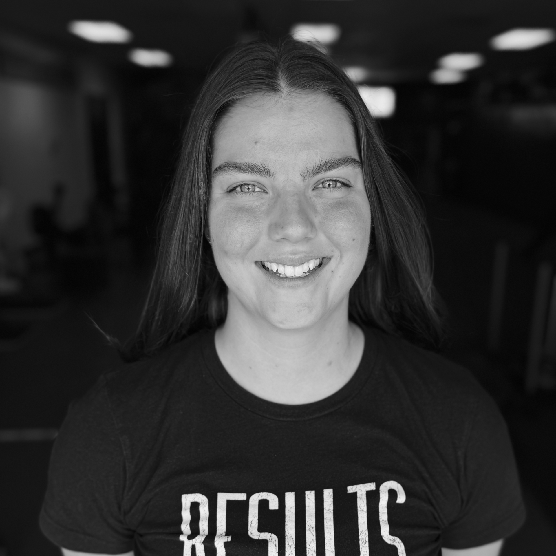 Smiling person in a black shirt with “RESULTS” text against a blurred dark background