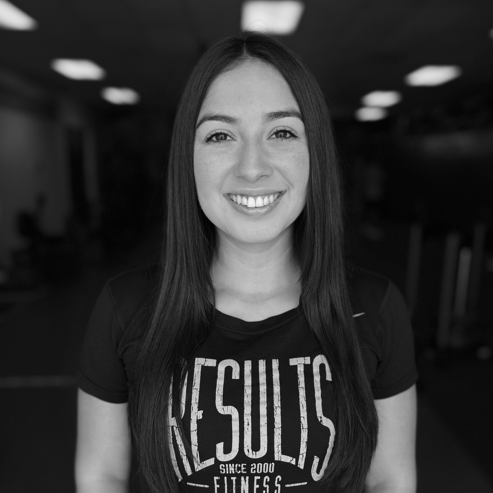 Smiling person in a dark “Results” T-shirt standing in a dim hallway