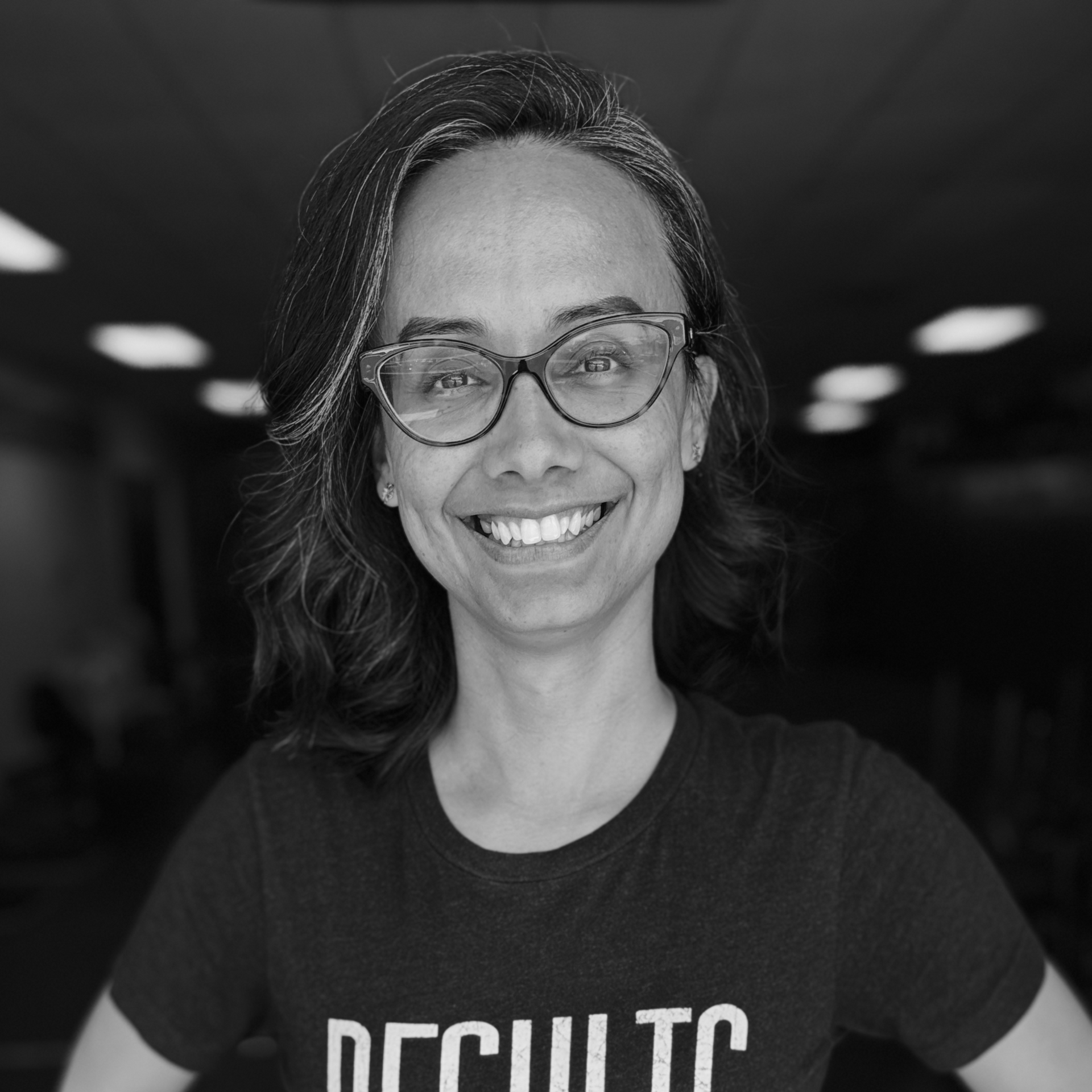 Smiling person wearing glasses and a dark T-shirt in a black-and-white portrait