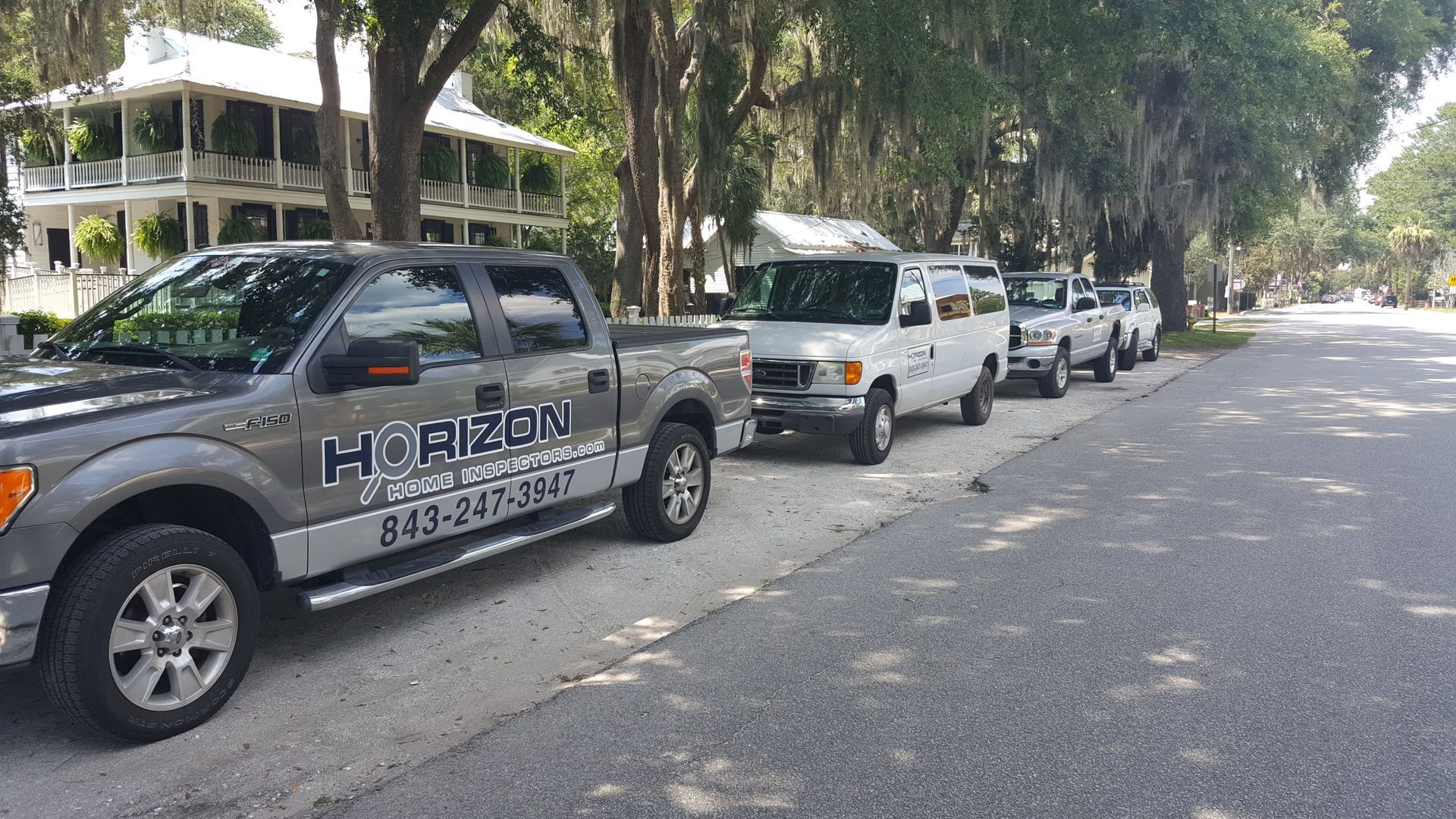 Parked cars lining a tree-shaded street, including a gray Horizon utility truck in front.