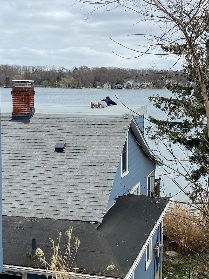 House by a lake with gray roof, chimney, and bare trees in winter