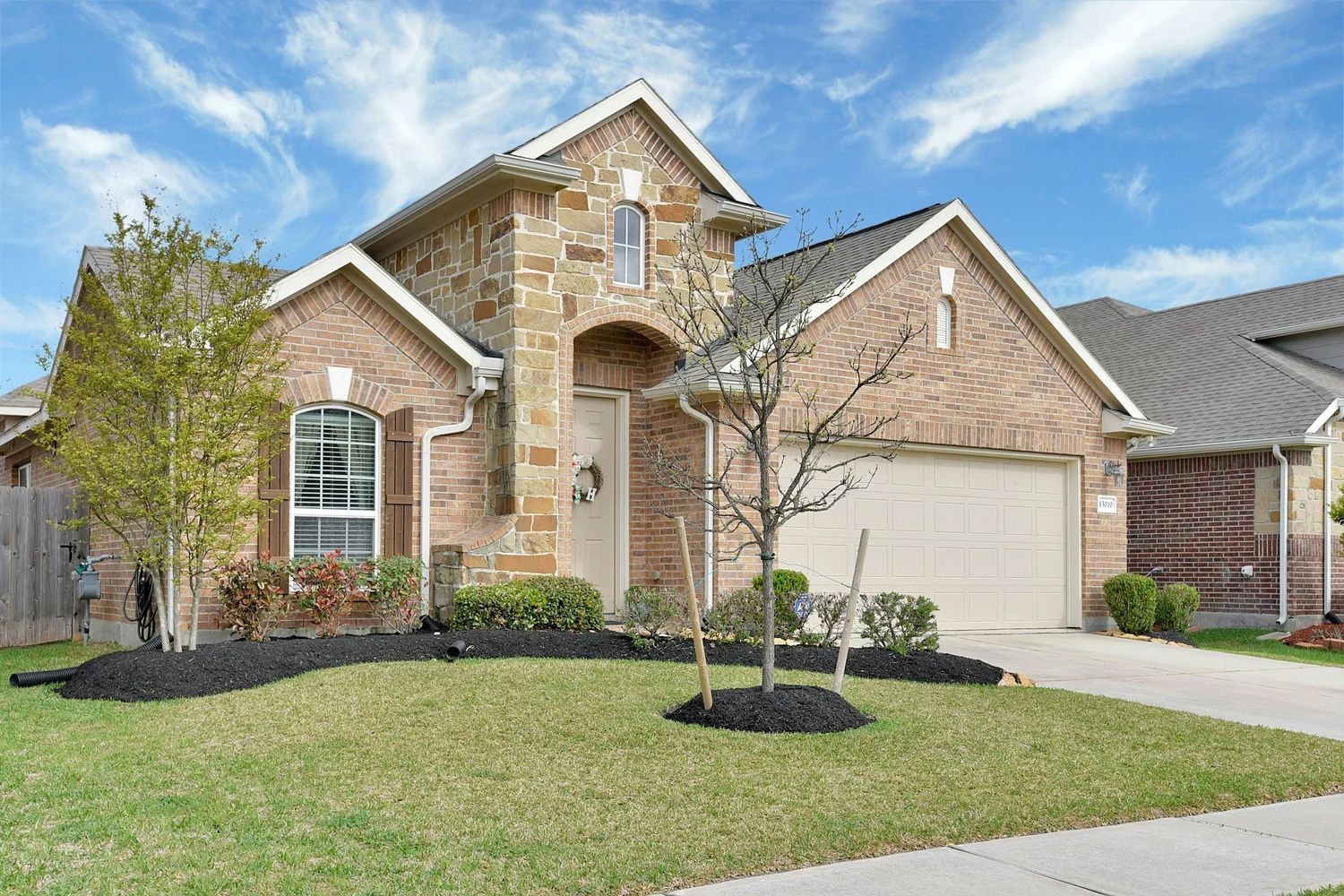 Brick suburban house with arched entry, two-car garage, and a manicured front lawn under a blue sky