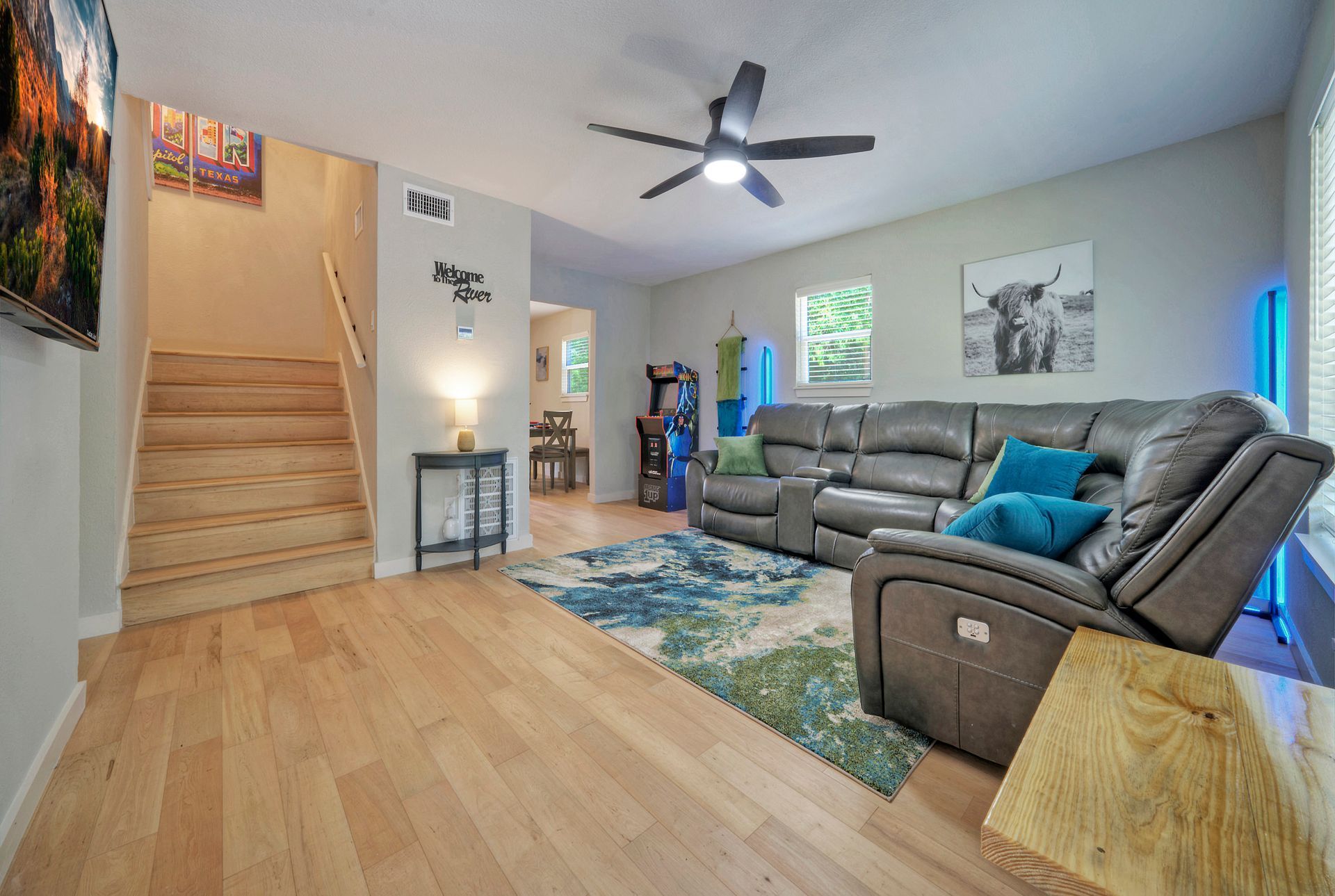 A living room with a couch , chair , stairs and a ceiling fan.