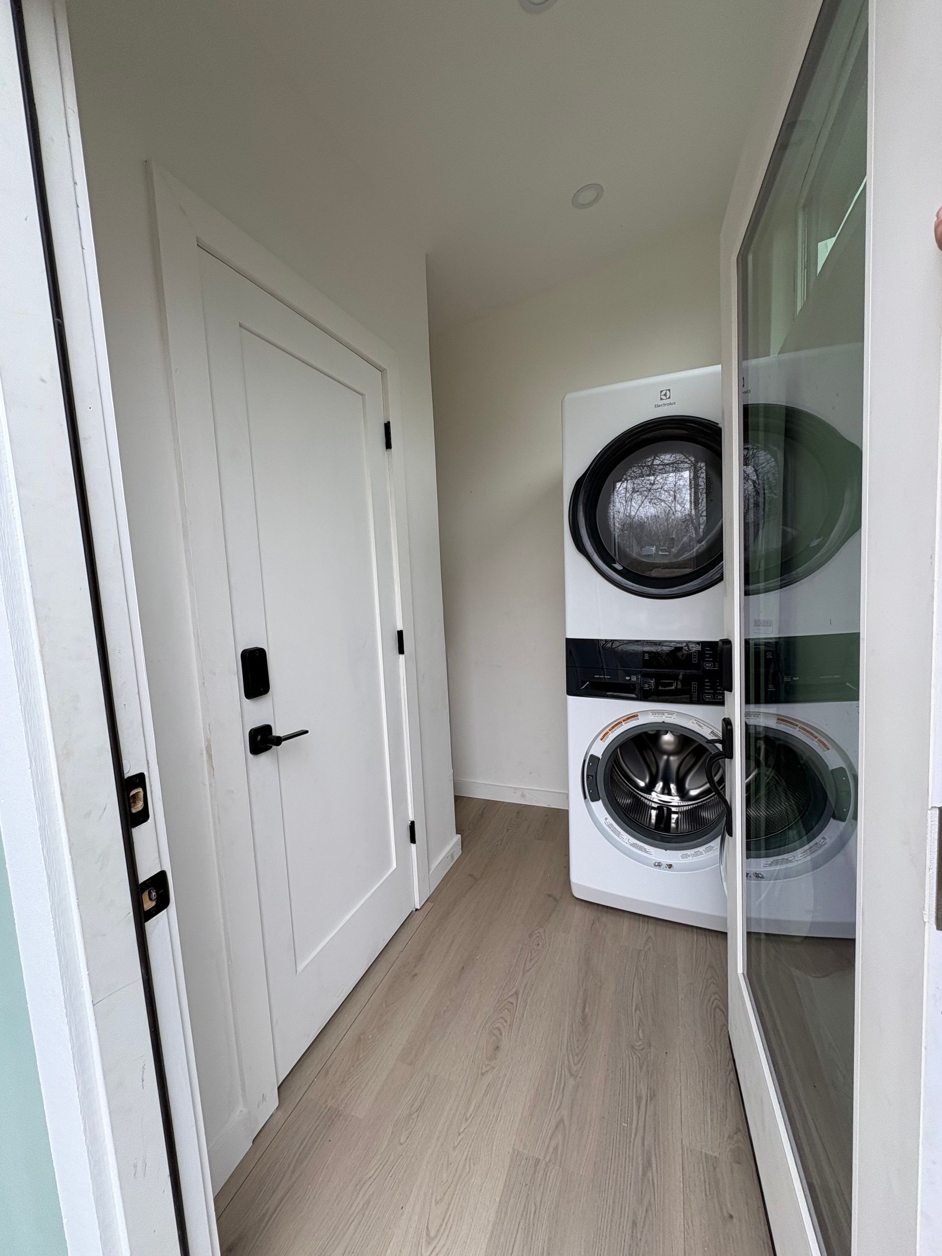 Narrow hallway with white doors and a stacked washer and dryer beside a mirrored closet.