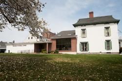 Large white house with a porch and attached garage, viewed from a grassy yard under a cloudy sky