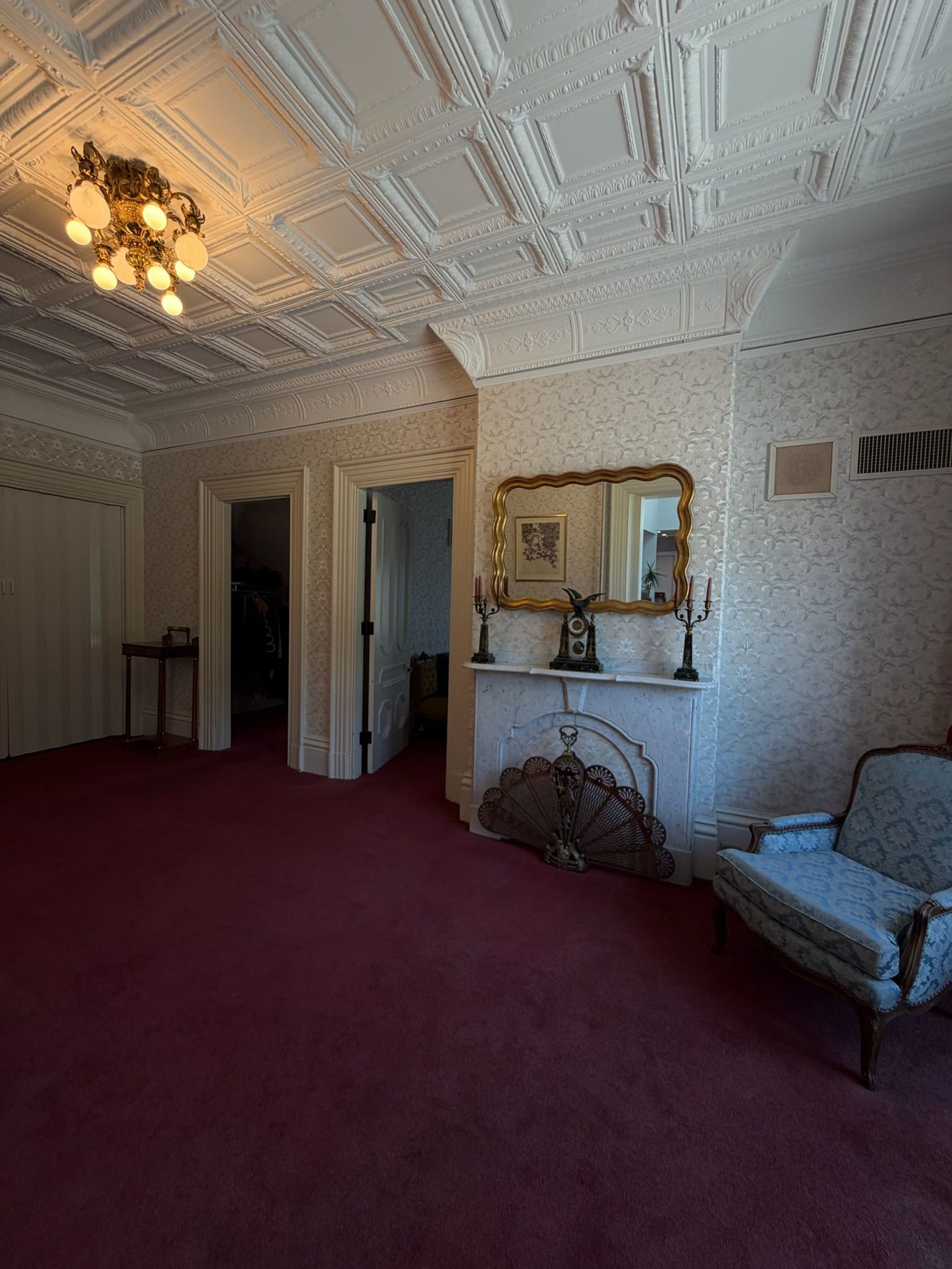 Elegant room with ornate white ceiling, red carpet, mirror, fireplace, and blue chair
