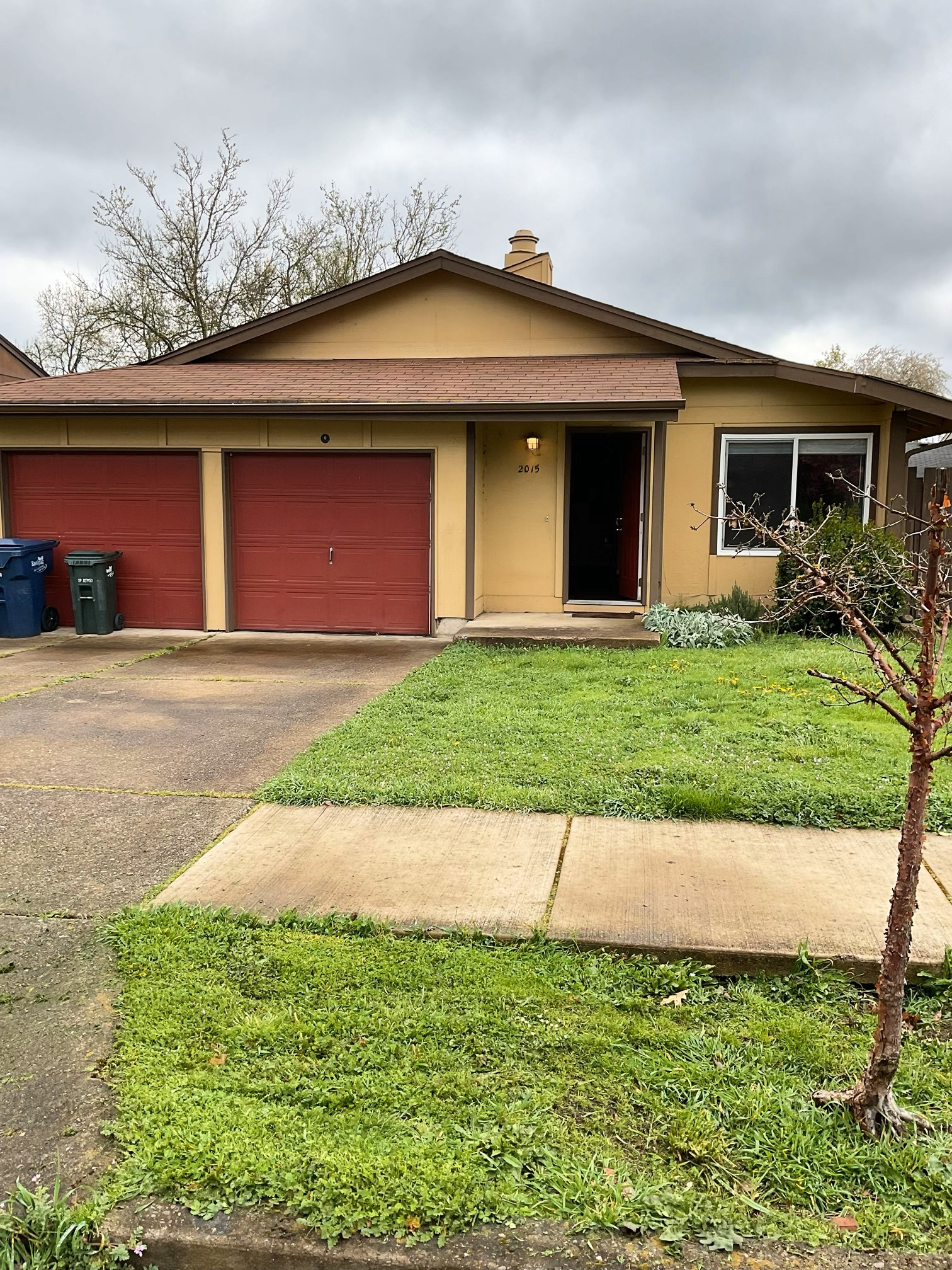 Tan house with red garage doors, green lawn, and overcast sky.