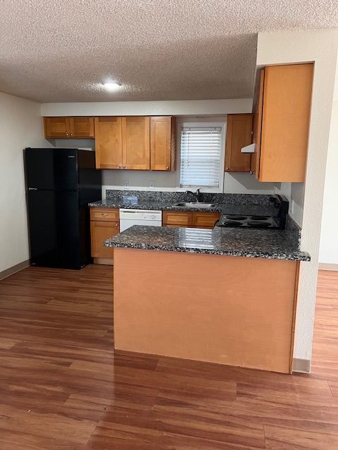 Kitchen with wood cabinets, granite countertops, black appliances, and hardwood floors.