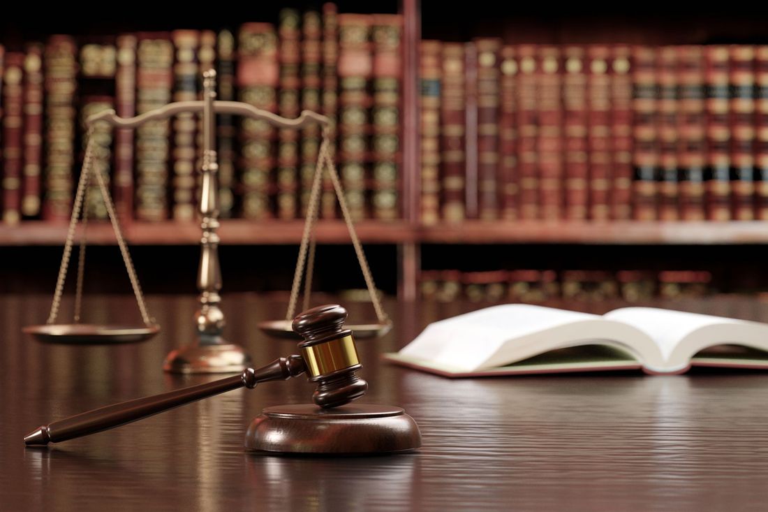 Libri di diritto, bilancia, martelletto del giudice e libro aperto su una scrivania in un'aula di tribunale.