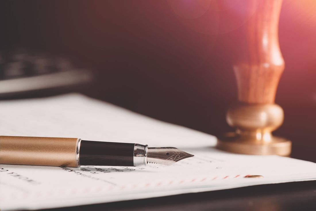 Penna stilografica su carta bianca accanto alla base di una lampada illuminata da una luce calda, pronta per scrivere.