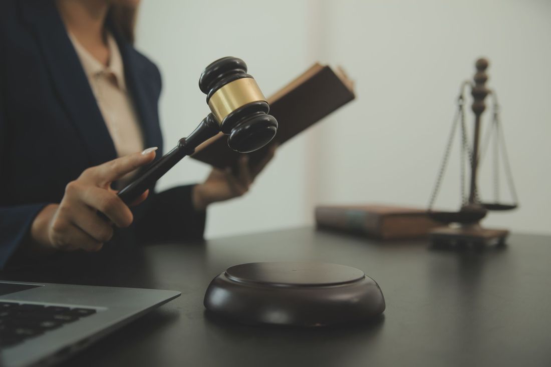 Un avvocato tiene in mano un martelletto sopra una scrivania con un computer portatile e una bilancia legale in un ufficio del tribunale.