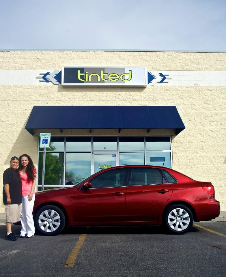 A red car is parked in front of a tinted store